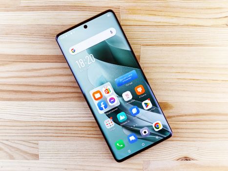 A sleek smartphone showing diverse apps on a bright wooden surface, showcasing technology in a top-view composition.